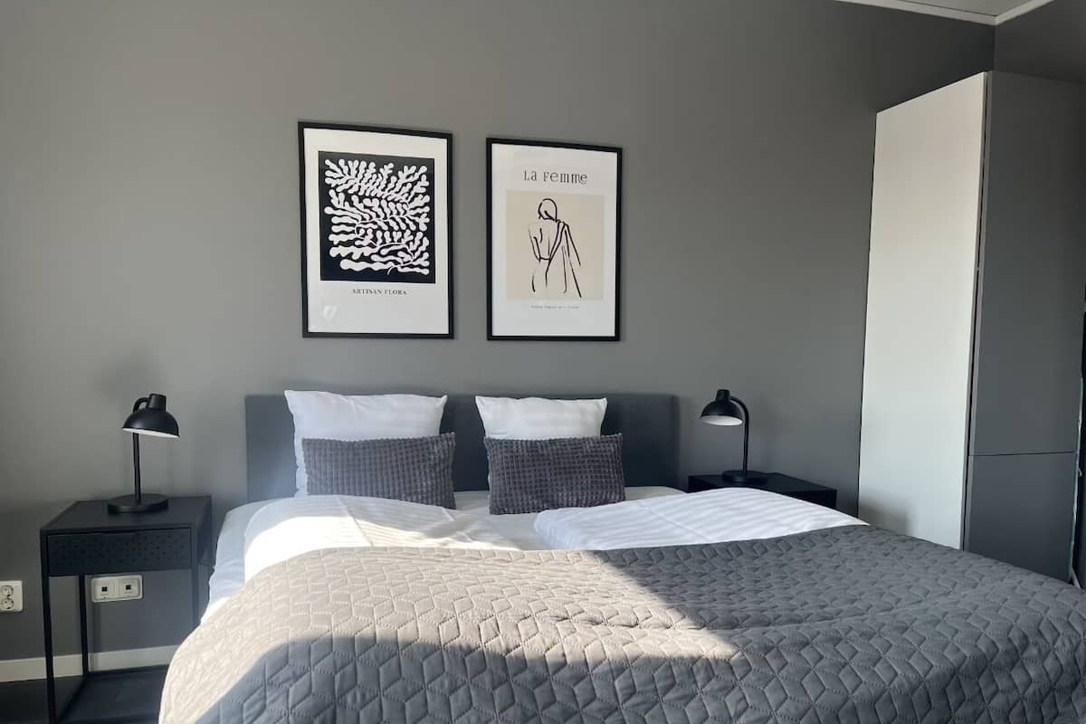 A modern hotel room with a large bed, two bedside tables, a wardrobe, and two framed artworks on the wall.
