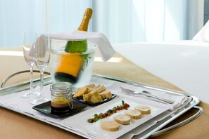 A tray with a bottle of champagne, glasses, and a dessert plate with various items. - NH Gijón (Gijon)
