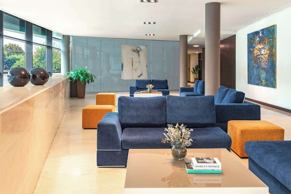 Un moderno hall de entrada con un conjunto de sofás azules, una mesa de centro con un jarrón y un cuadro abstracto de gran tamaño en la pared.