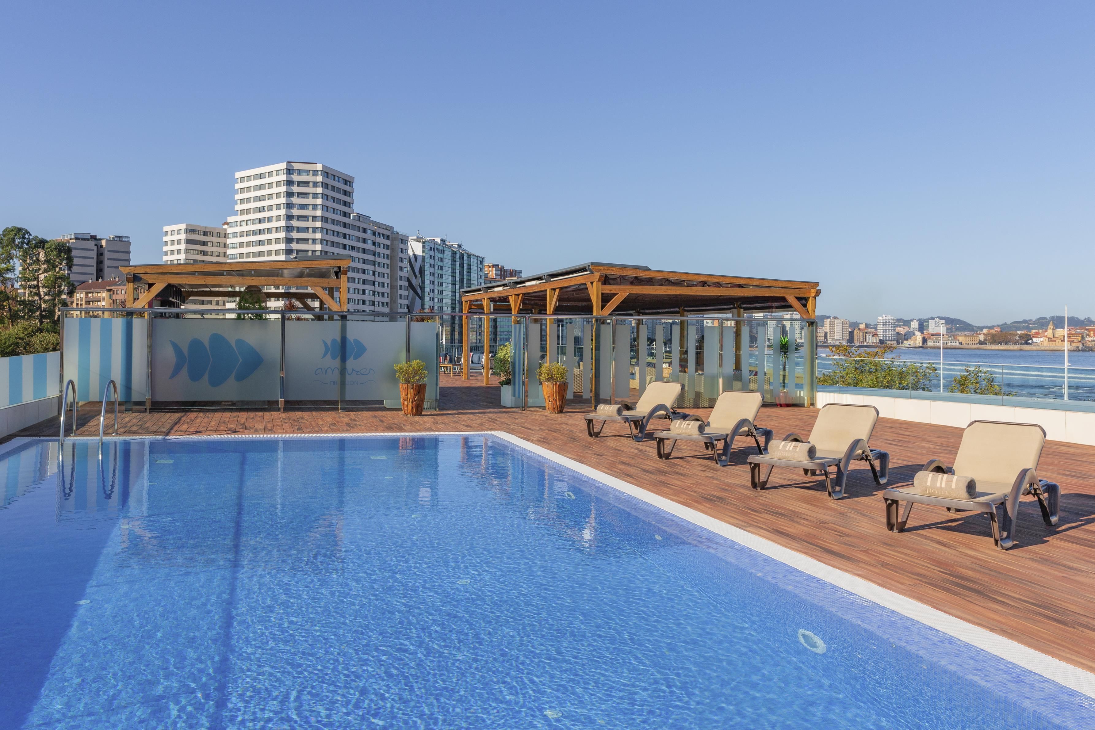 A rooftop pool with lounge chairs and a view of the city skyline.