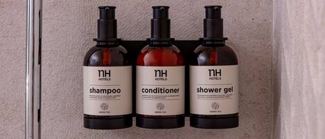 Tres botellas de artículos de baño de hotel (champú, acondicionador, gel de ducha) en una pared.