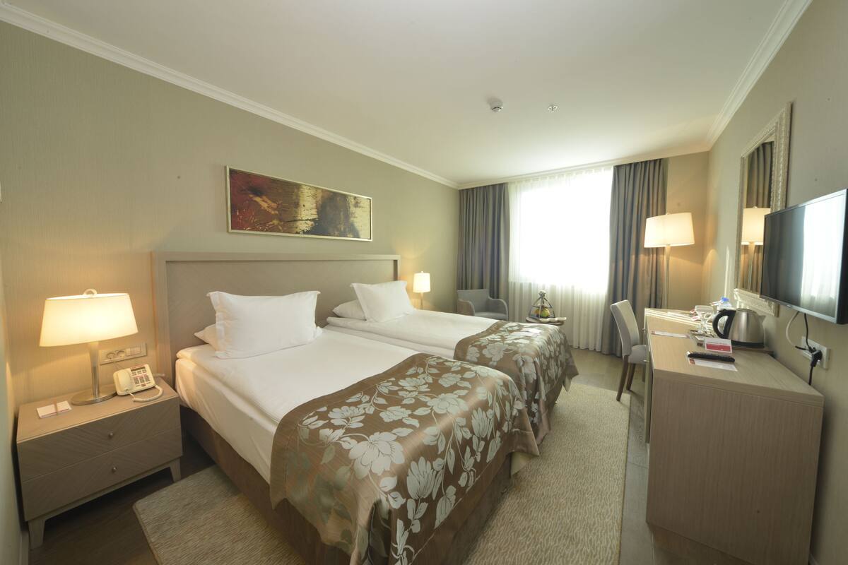 A hotel room with two beds, a desk with a TV, a lamp, and a painting on the wall.