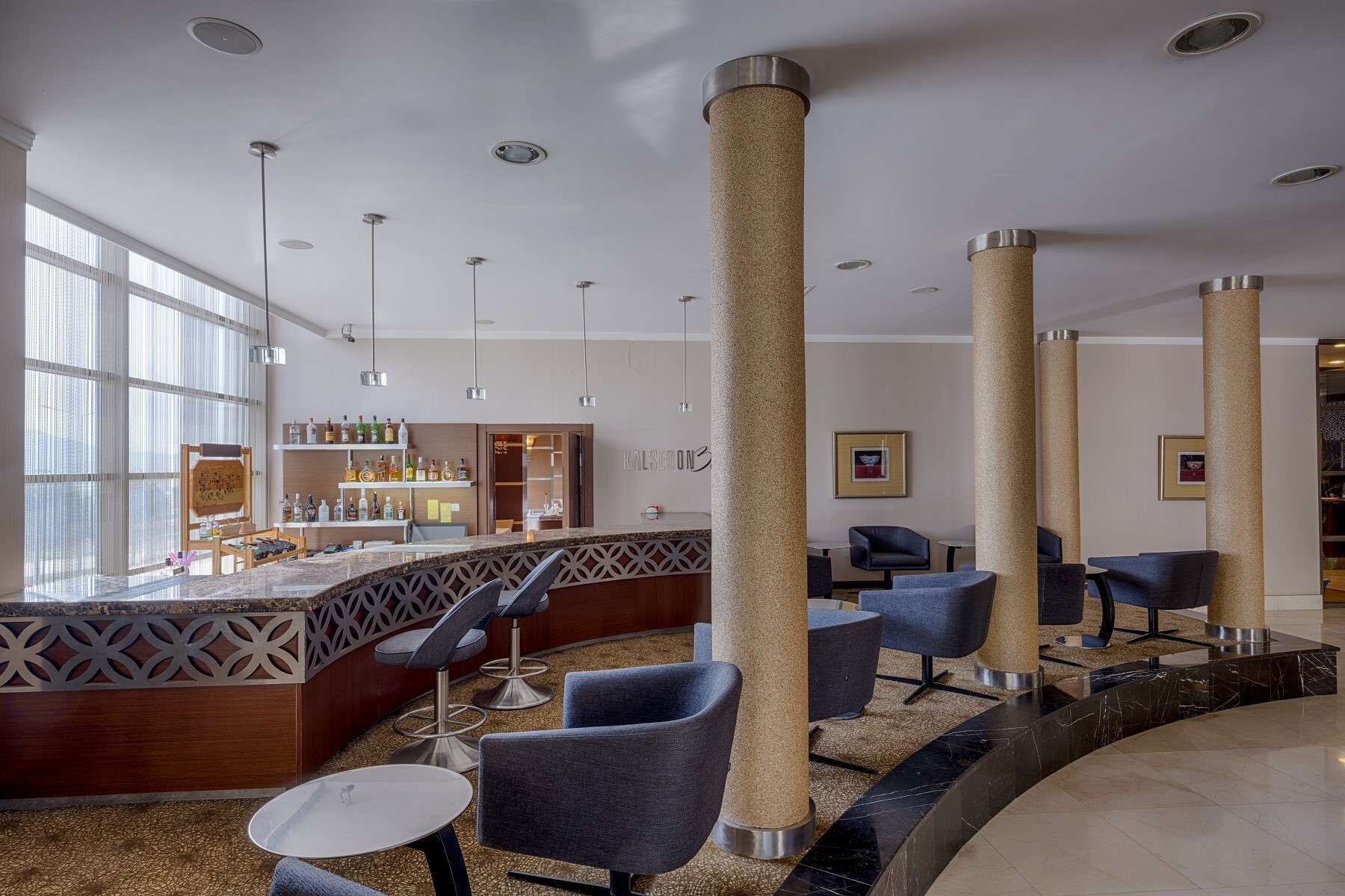 A modern lobby with a bar area, seating, and tall columns.