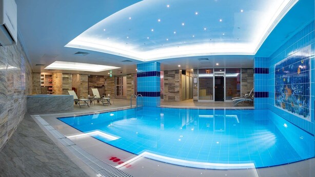 Una piscina interior moderna con agua cristalina, rodeada de paredes de azulejos azules y un techo curvo con iluminación empotrada.