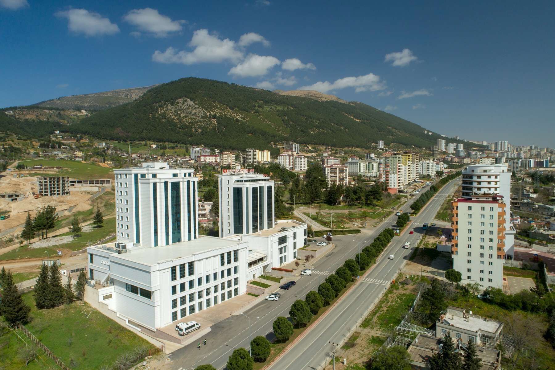 A modern building complex with multiple high-rise structures, a central road, and a mountainous backdrop.