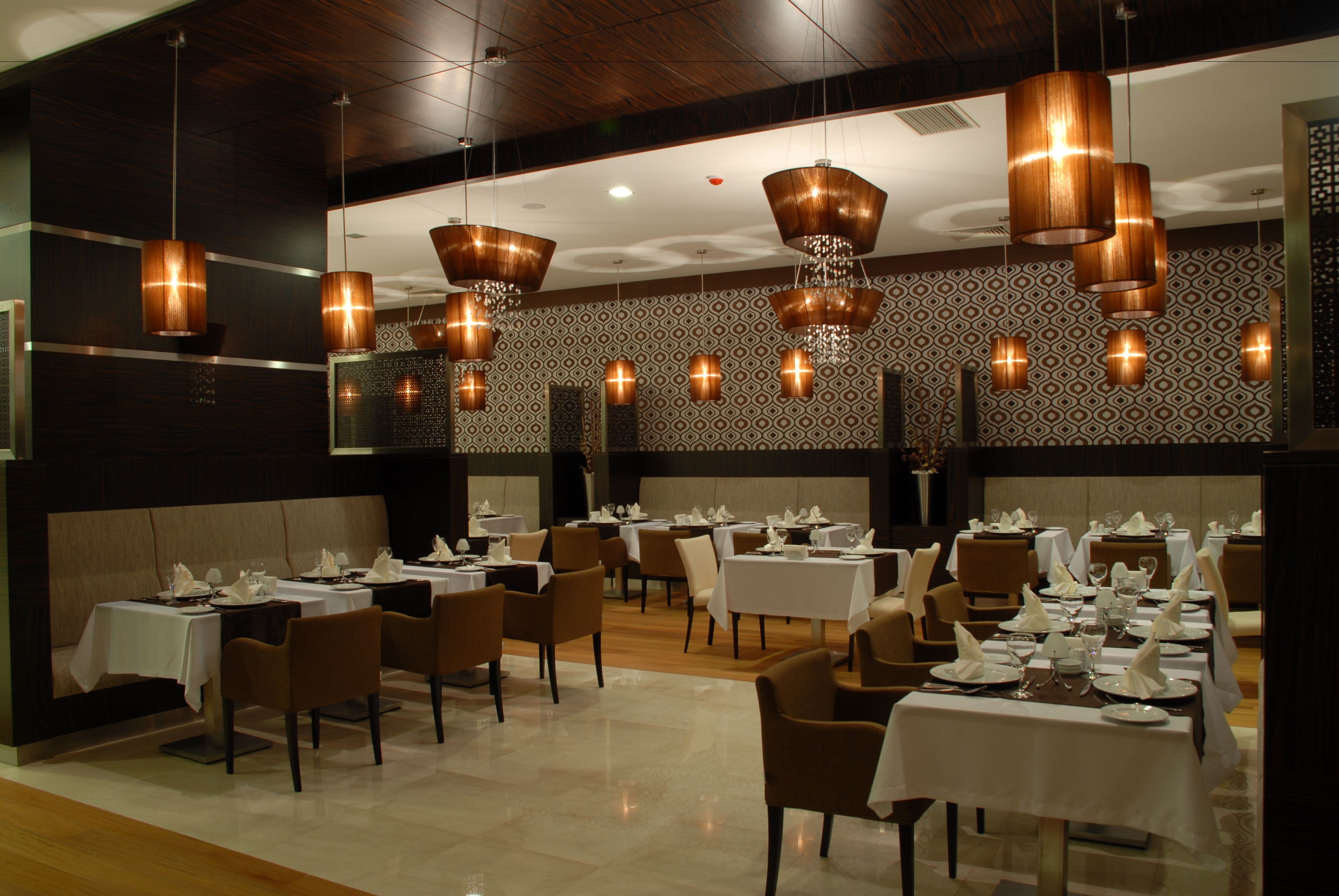 Un restaurante con varias mesas preparadas para comer, con una pared decorada y lámparas colgantes de cobre.