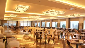 Un comedor amplio con varias mesas y sillas, ventanas grandes y modernas lámparas de techo.