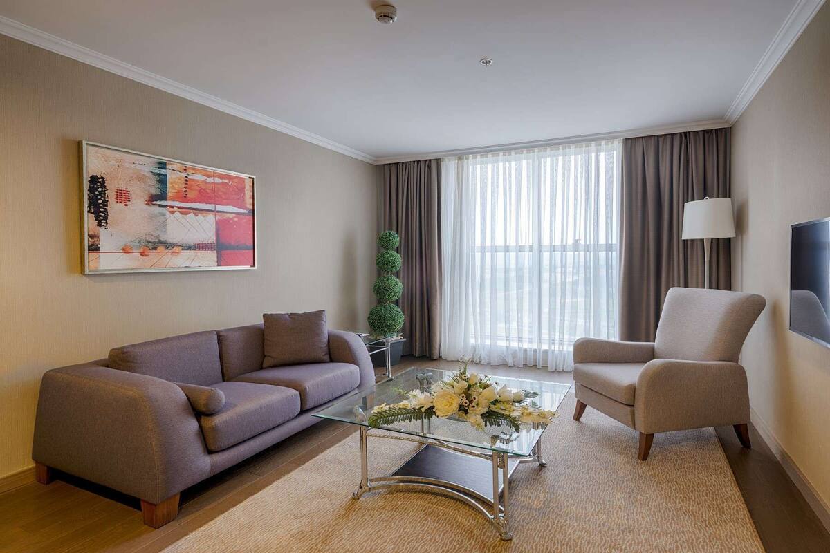 A modern living room with a sofa, armchair, glass coffee table, and a painting on the wall.