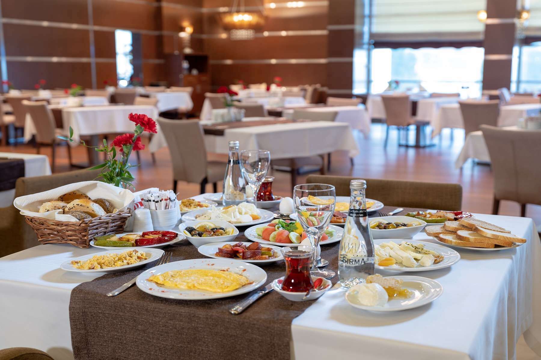 A dining area with multiple tables set for breakfast, featuring a variety of dishes and beverages.