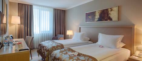 A hotel room with two beds, a desk with a lamp, a telephone, and a painting on the wall.
