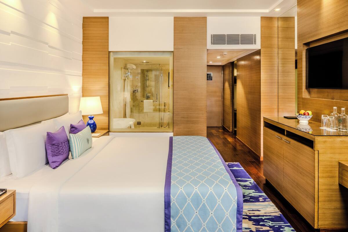 A hotel room with a large bed, a TV, a desk, and a shower area.