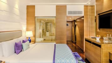 A hotel room with a large bed, a TV, a desk, and a shower area.