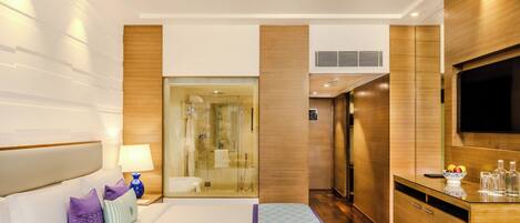 A hotel room with a large bed, a TV, a desk, and a shower area.