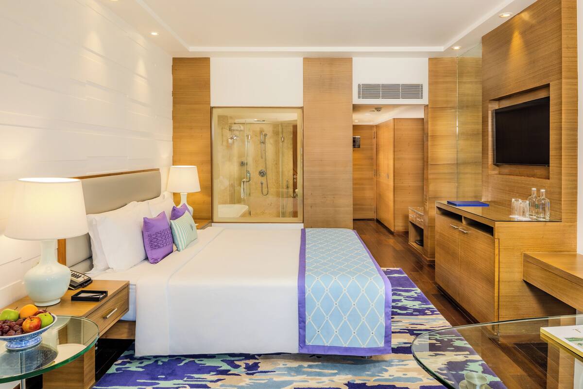 A modern hotel room with a large bed, bedside table with lamp, and a glass shower enclosure.