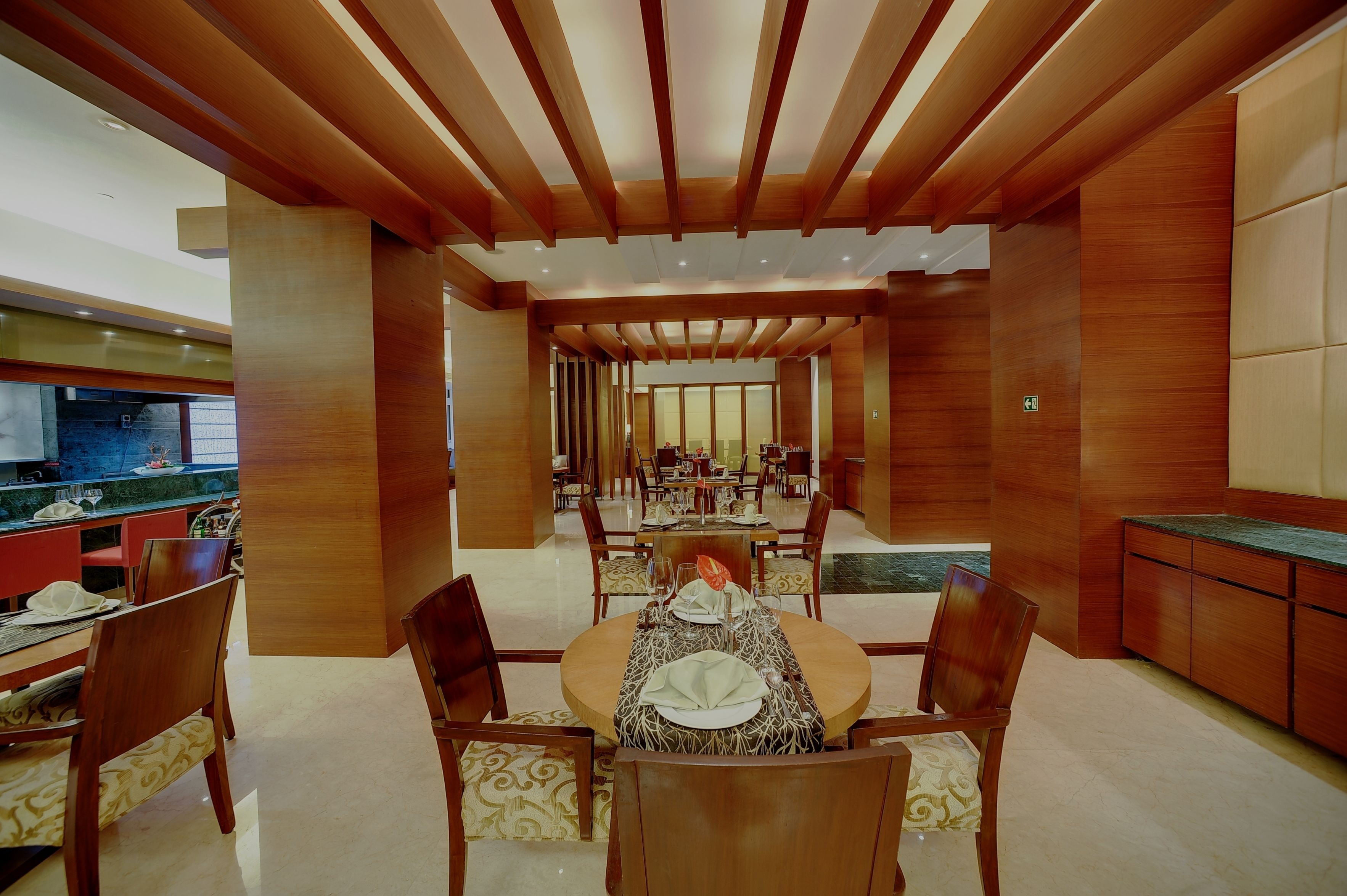 A spacious dining area with wooden beams, a central round table set for four, and a view into a dining hall.