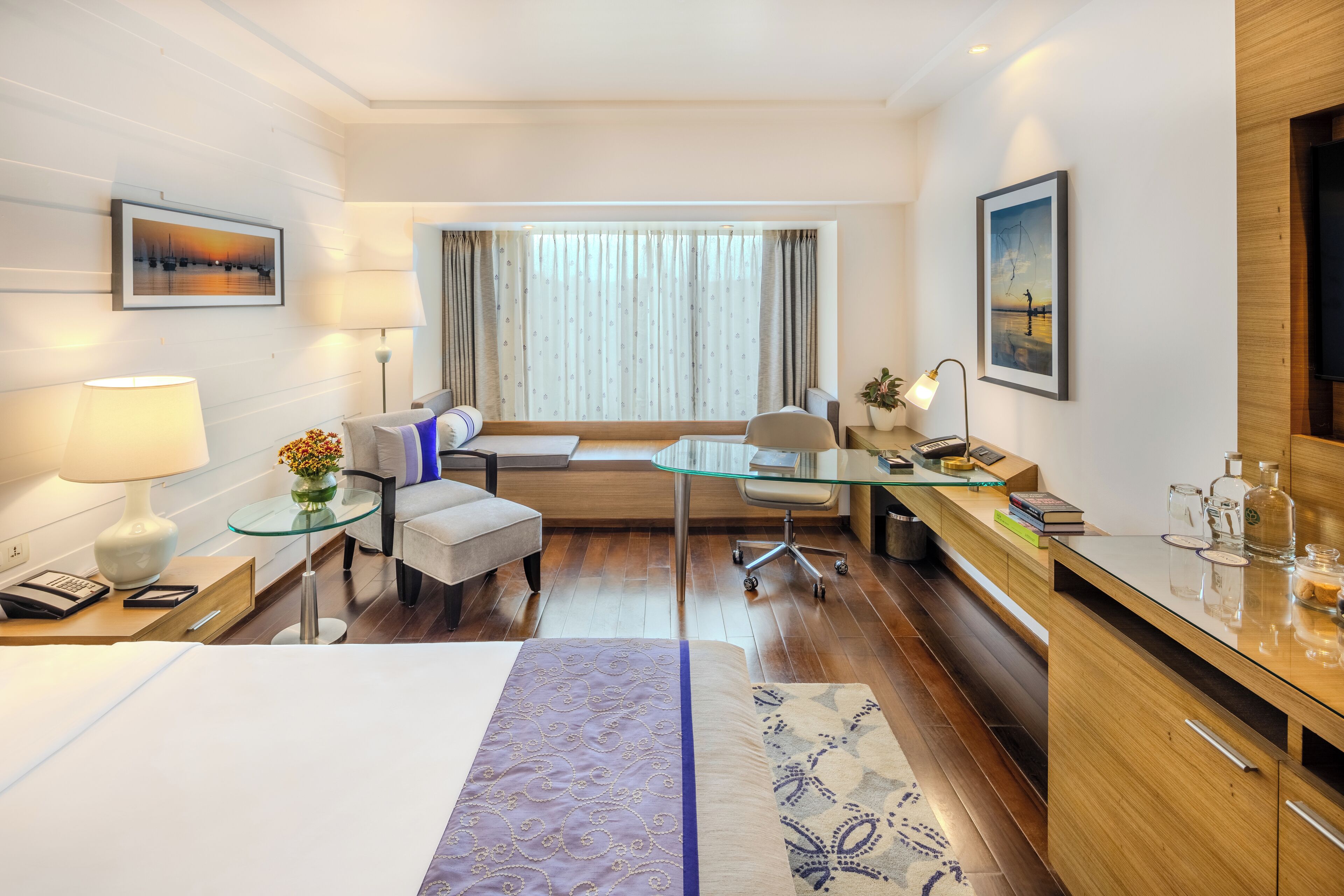 A modern hotel room with a bed, a desk, a chair, a sofa, and a TV.