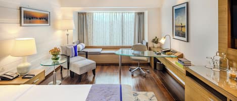 Una habitación de hotel moderna con cama, escritorio, silla, sofá y televisor.