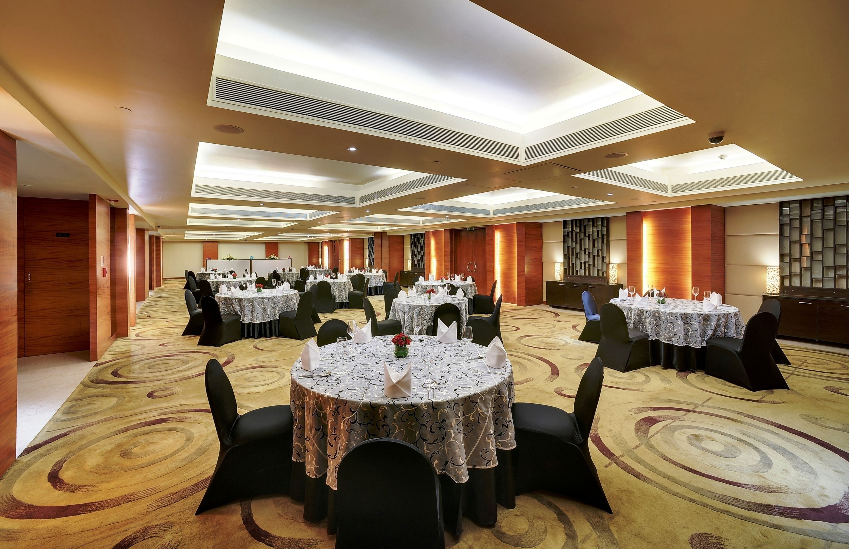 Un amplio salón de banquetes con varias mesas redondas dispuestas para cenar, equipado con sillas y vajilla.