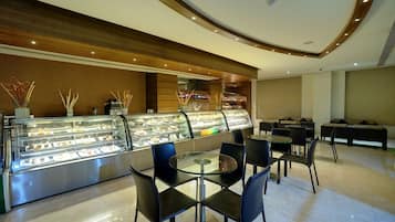 A modern cafe with a glass display case filled with pastries and desserts, black chairs, and a wooden ceiling.