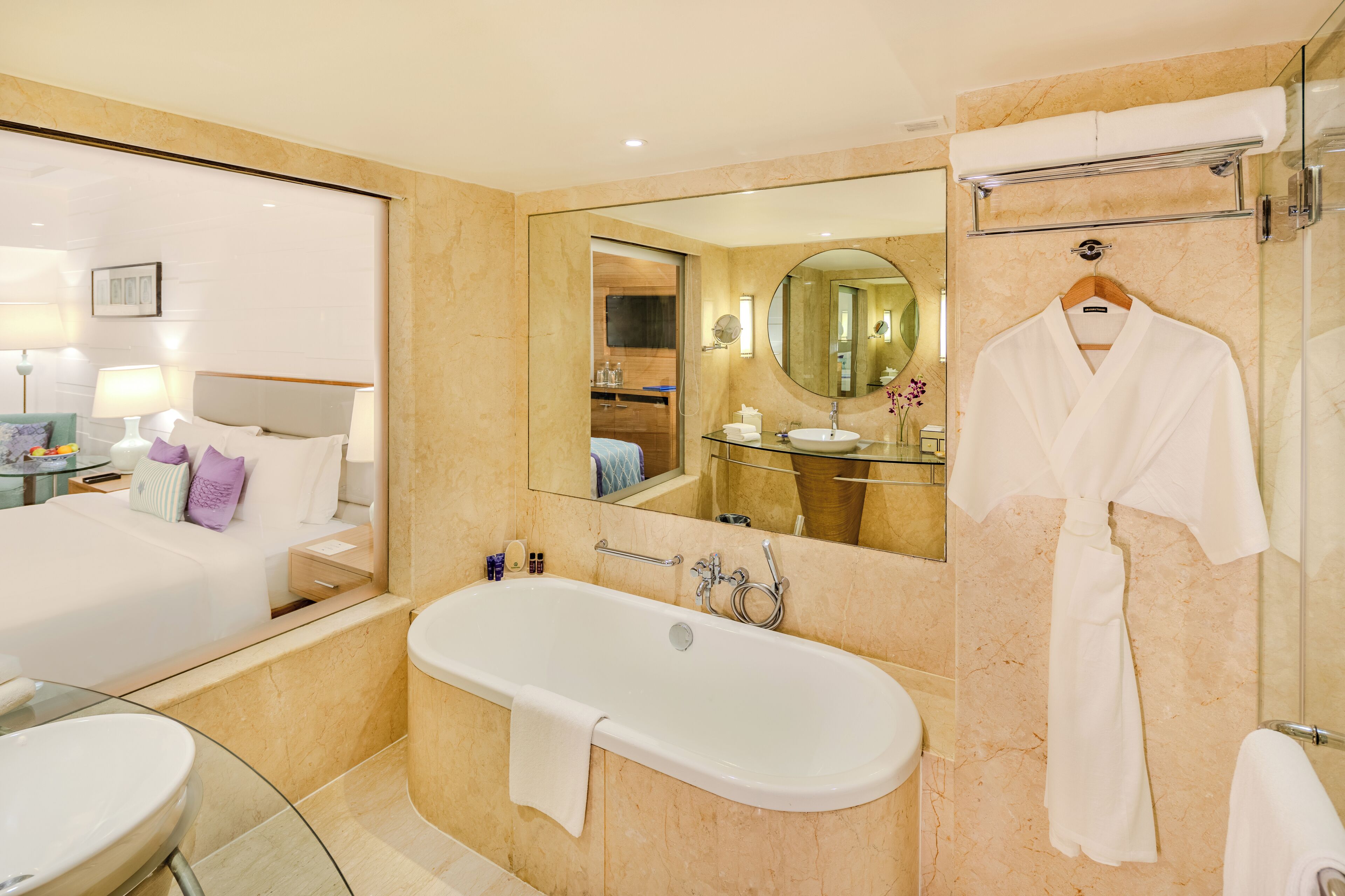 A modern hotel bathroom with a large bathtub, a glass-enclosed sink, and a walk-in shower.