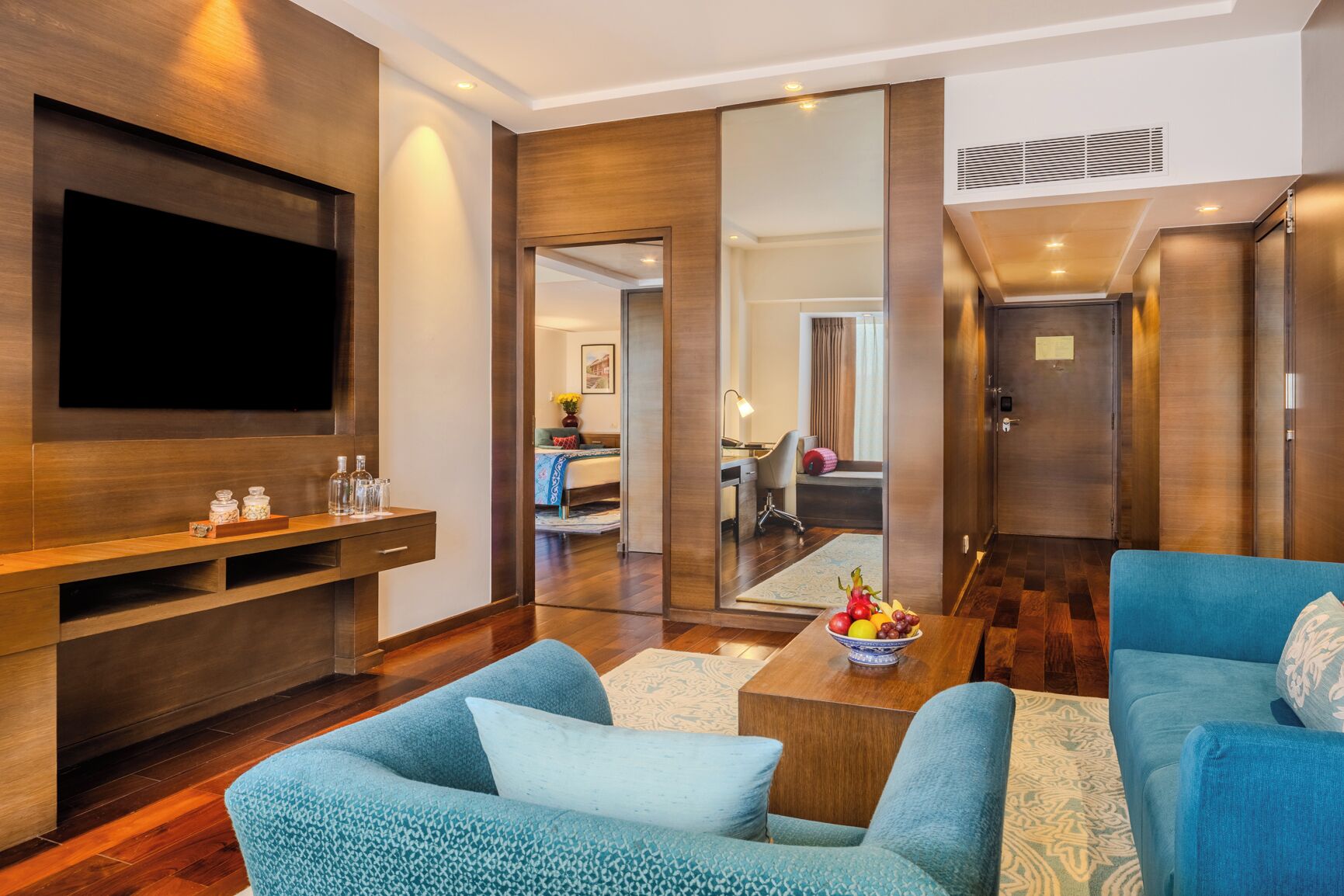 A modern living room with a flat-screen TV, blue sofas, a coffee table with fruit, and a wooden entertainment unit.