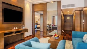 A modern living room with a flat-screen TV, blue sofas, a coffee table with fruit, and a wooden entertainment unit.