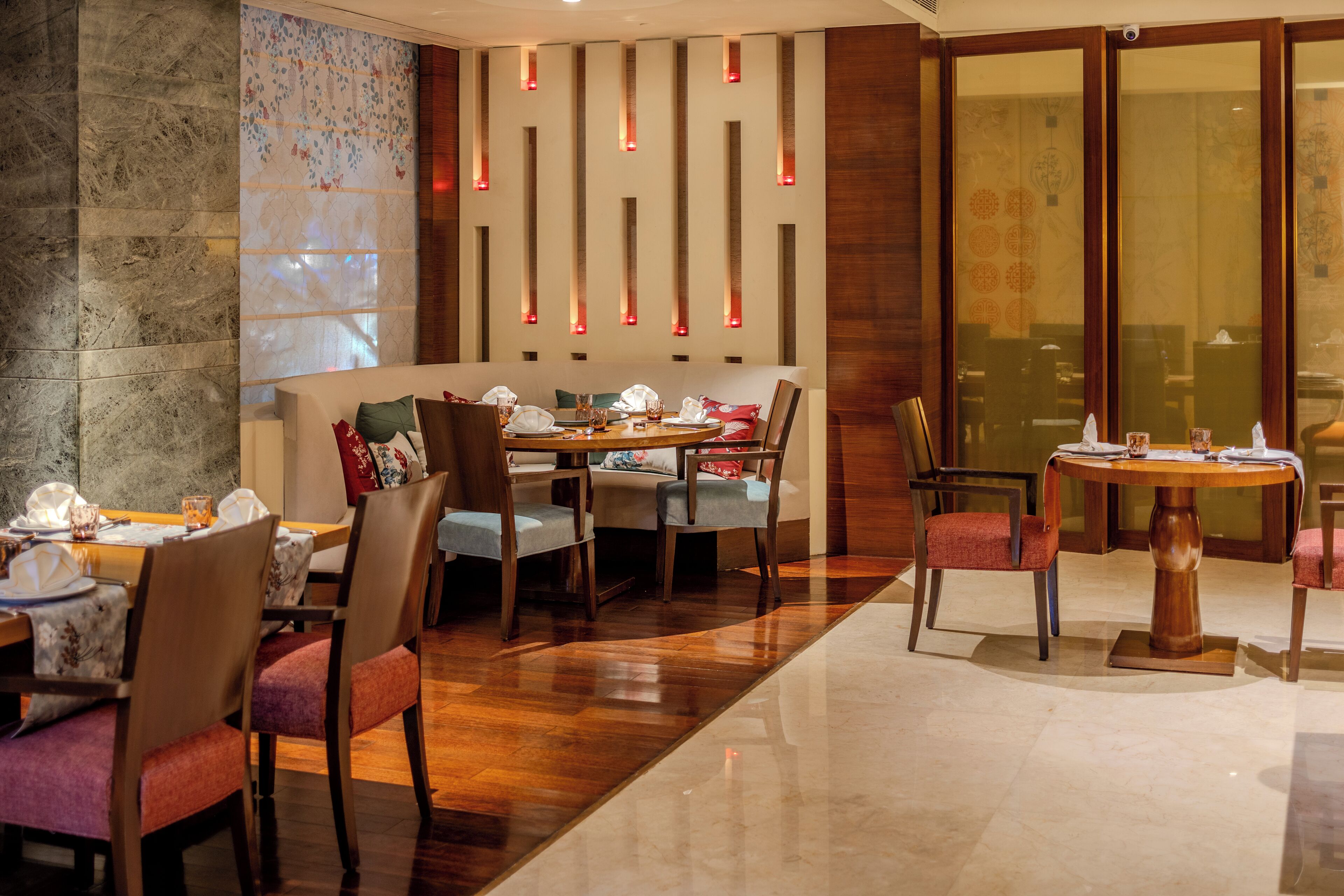 Un comedor con mesas y sillas de madera, una pared decorativa con luminarias verticales y una zona de estar con un banco acolchado.
