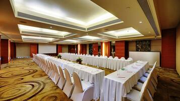 A conference room with long tables, white chairs, and a carpeted floor.
