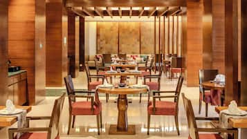 Un amplio comedor de hotel con varias mesas y sillas redondas, paneles de madera y un diseño interior moderno.