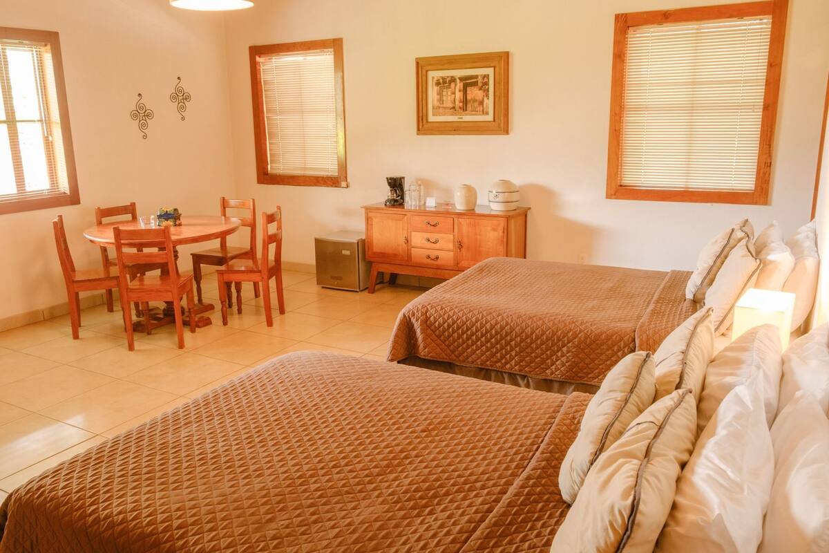 Ein Hotelzimmer mit zwei Betten, einem Holztisch, Stühlen, einem Schrank und einem Bild an der Wand.