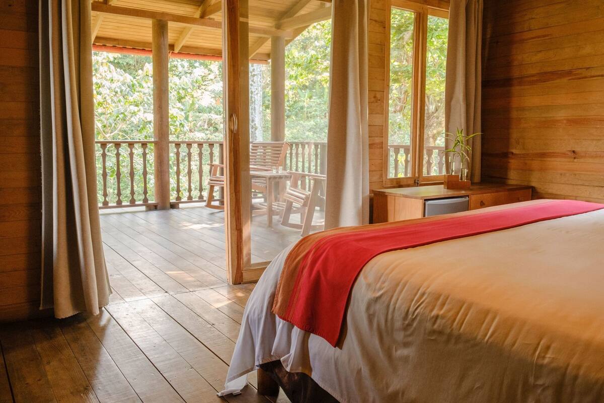 Ein Zimmer mit Holzboden, einem Bett, einem Schreibtisch und einem Balkon mit Stühlen.