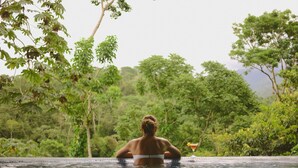 Una persona relajándose en una piscina con una bebida, rodeada de exuberante vegetación.
