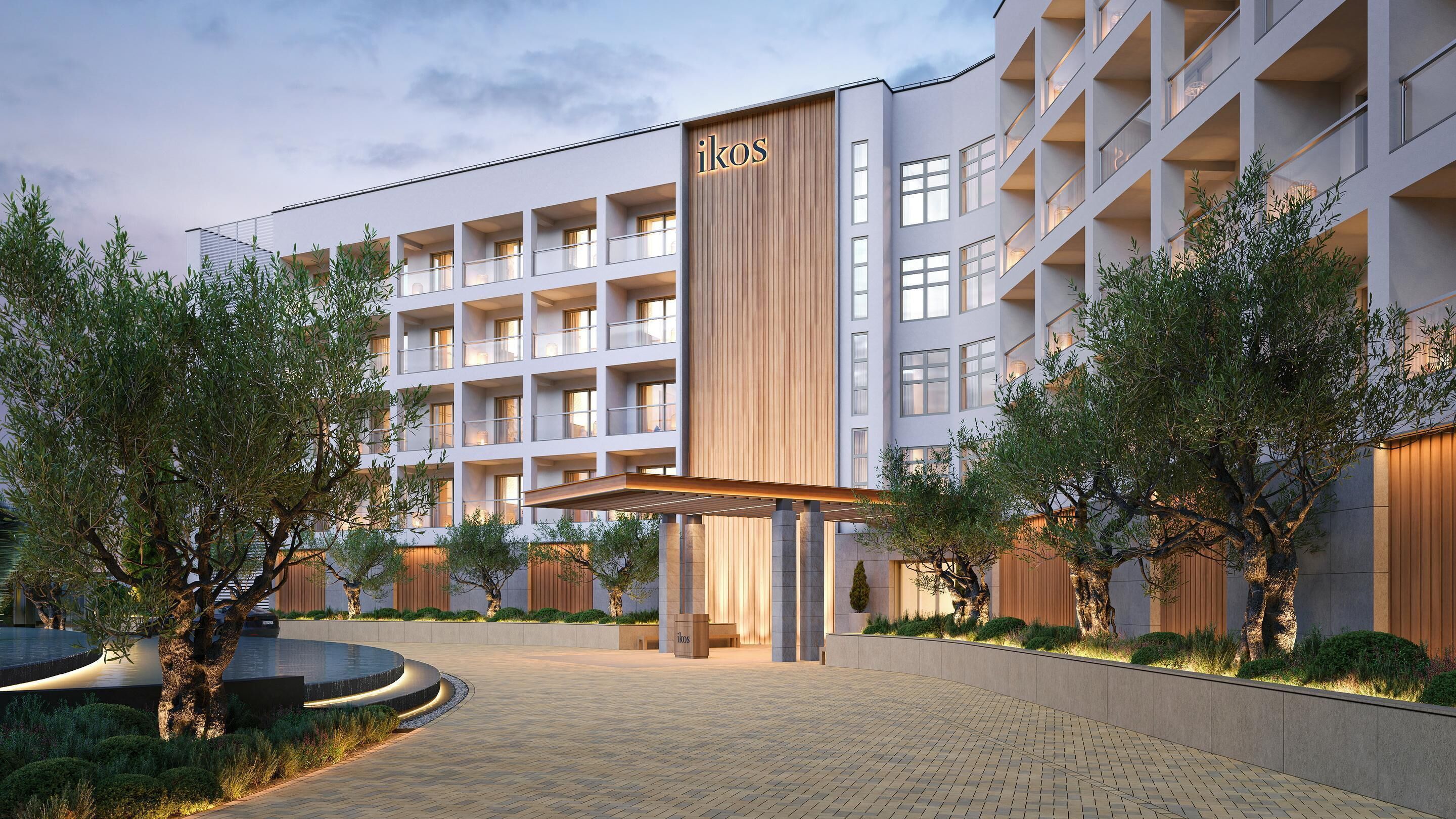 A modern hotel with a central entrance, multiple balconies, and a well-maintained garden area.