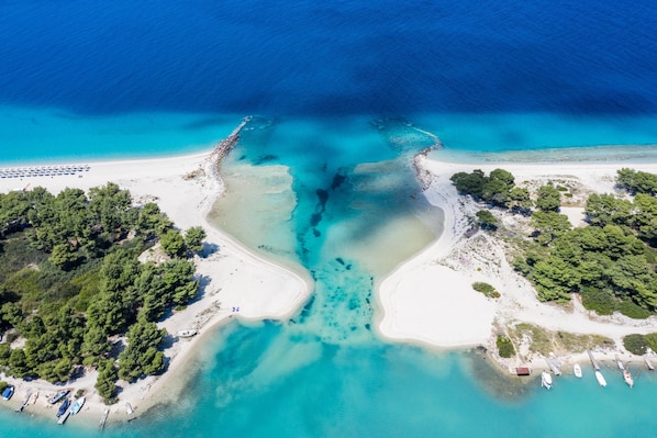 An aerial view of a coastal area with clear turquoise waters, sandy beaches, and dense green vegetation.