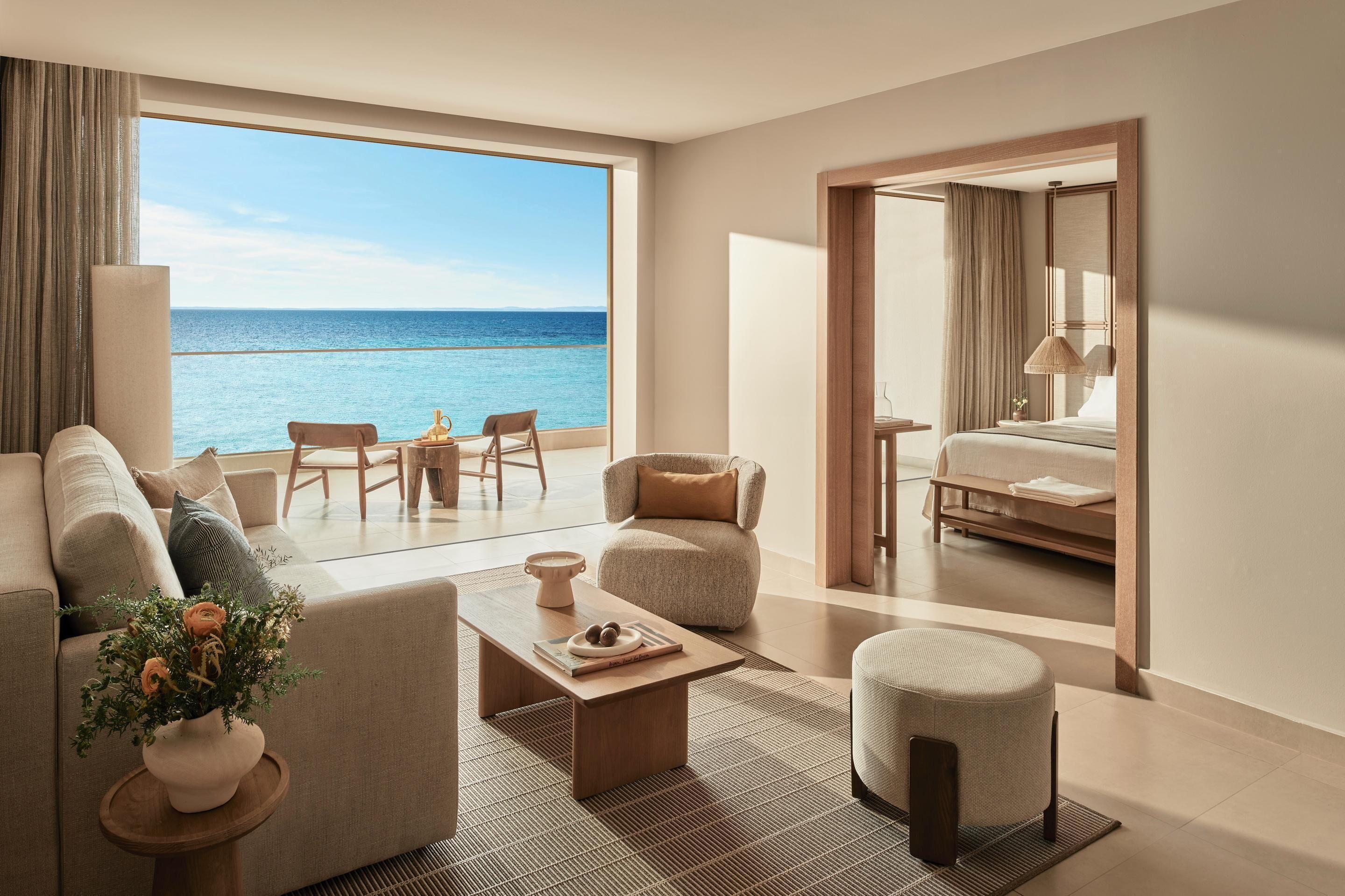 A modern hotel room with a large balcony, a sofa, a coffee table, and a view of the ocean.
