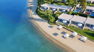 An aerial view of a coastal hotel with beachfront rooms, a swimming pool, and a clear blue sea.