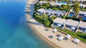 Vista aérea de un hotel frente al mar con villas privadas en la playa, una piscina y una playa de arena.