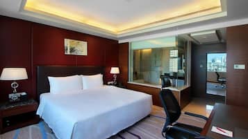 A hotel room with a large bed, two bedside tables with lamps, a desk with a chair, and a large window offering a city view.