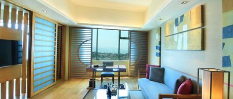 A modern living room with a sofa, coffee table, and a TV. There is a balcony with a view.
