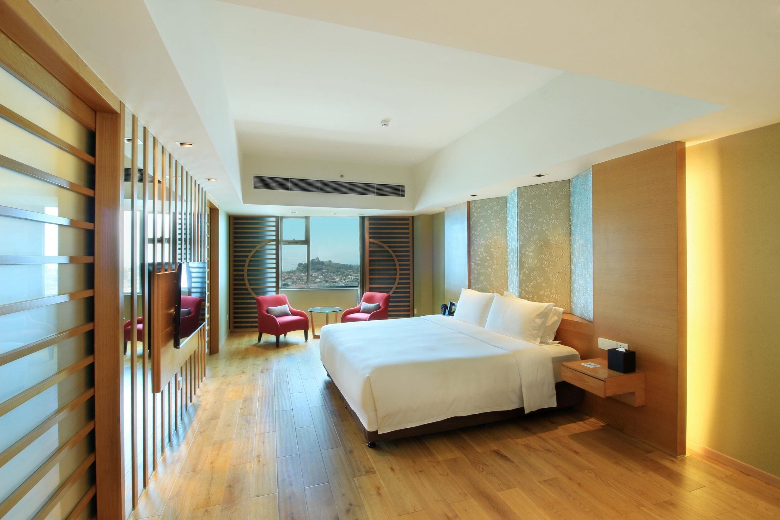A modern hotel room with a large bed, a small desk, a chair, and a view of the outdoors.