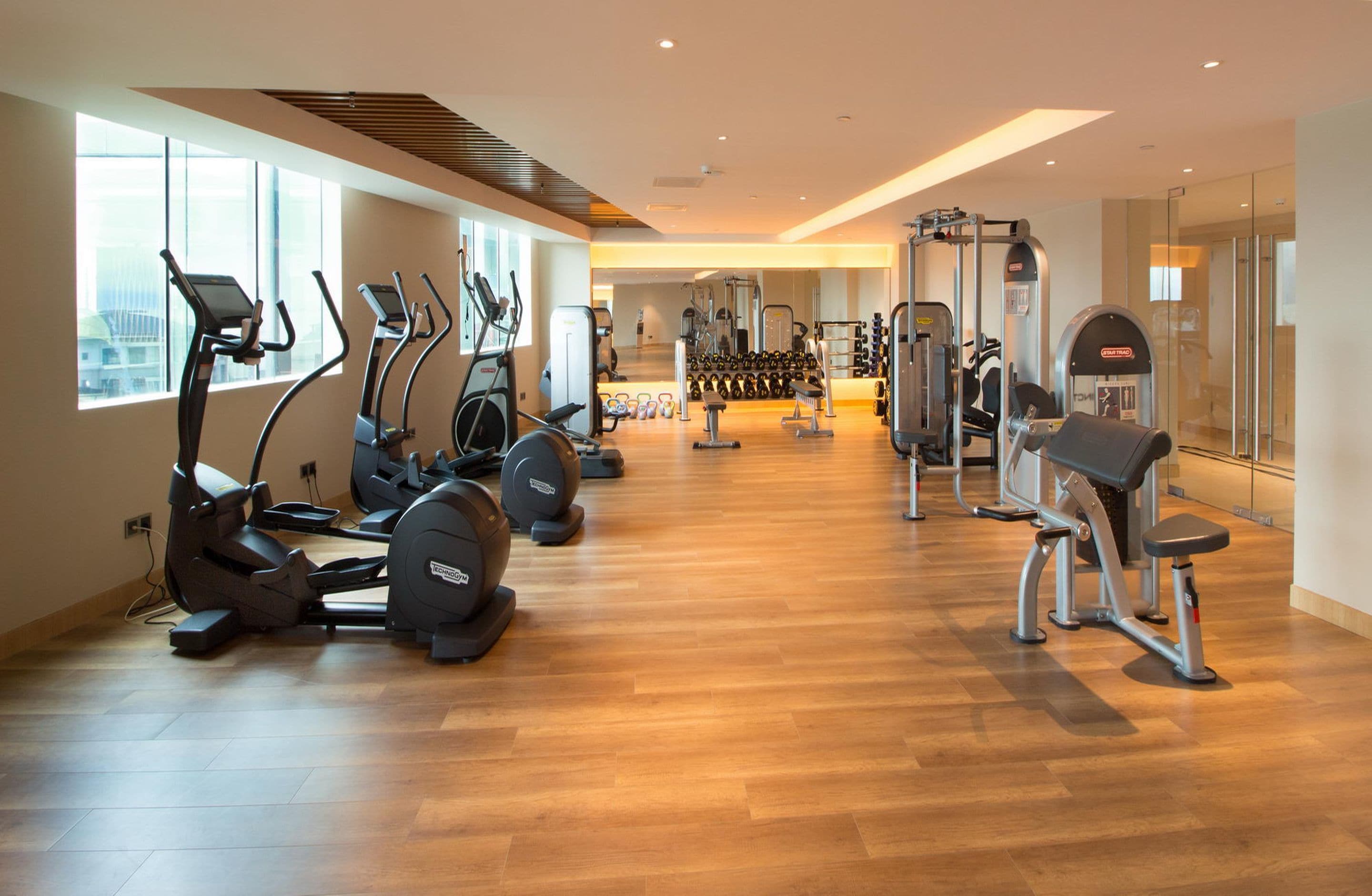 Un gimnasio con cintas de correr, elípticas, pesas libres y un muro de espejos.