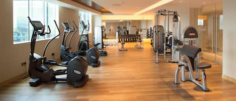 A gym with treadmills, elliptical machines, free weights, and a mirror wall.