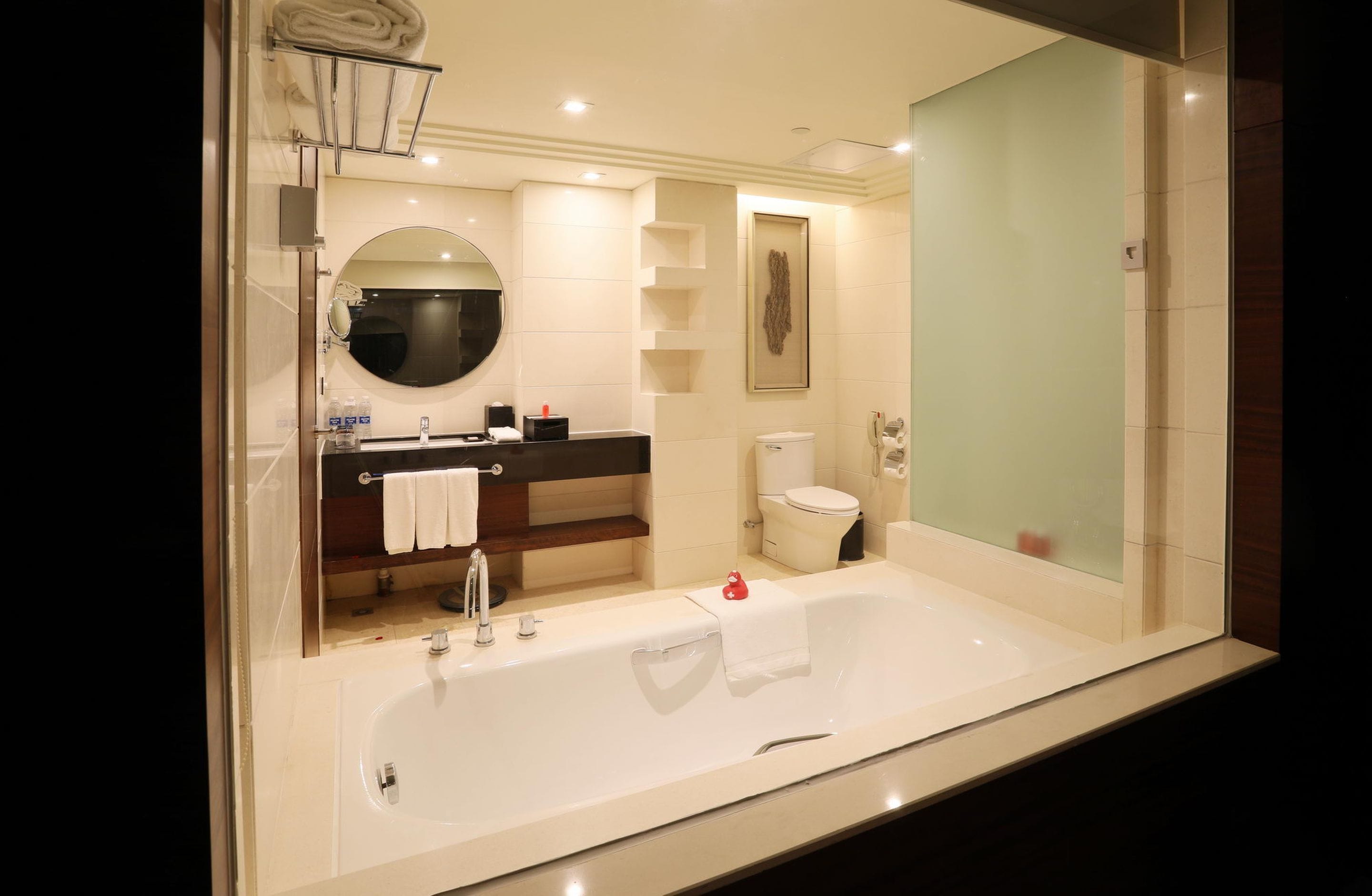 A modern bathroom with a large bathtub, a round mirror, a toilet, and a shower area.