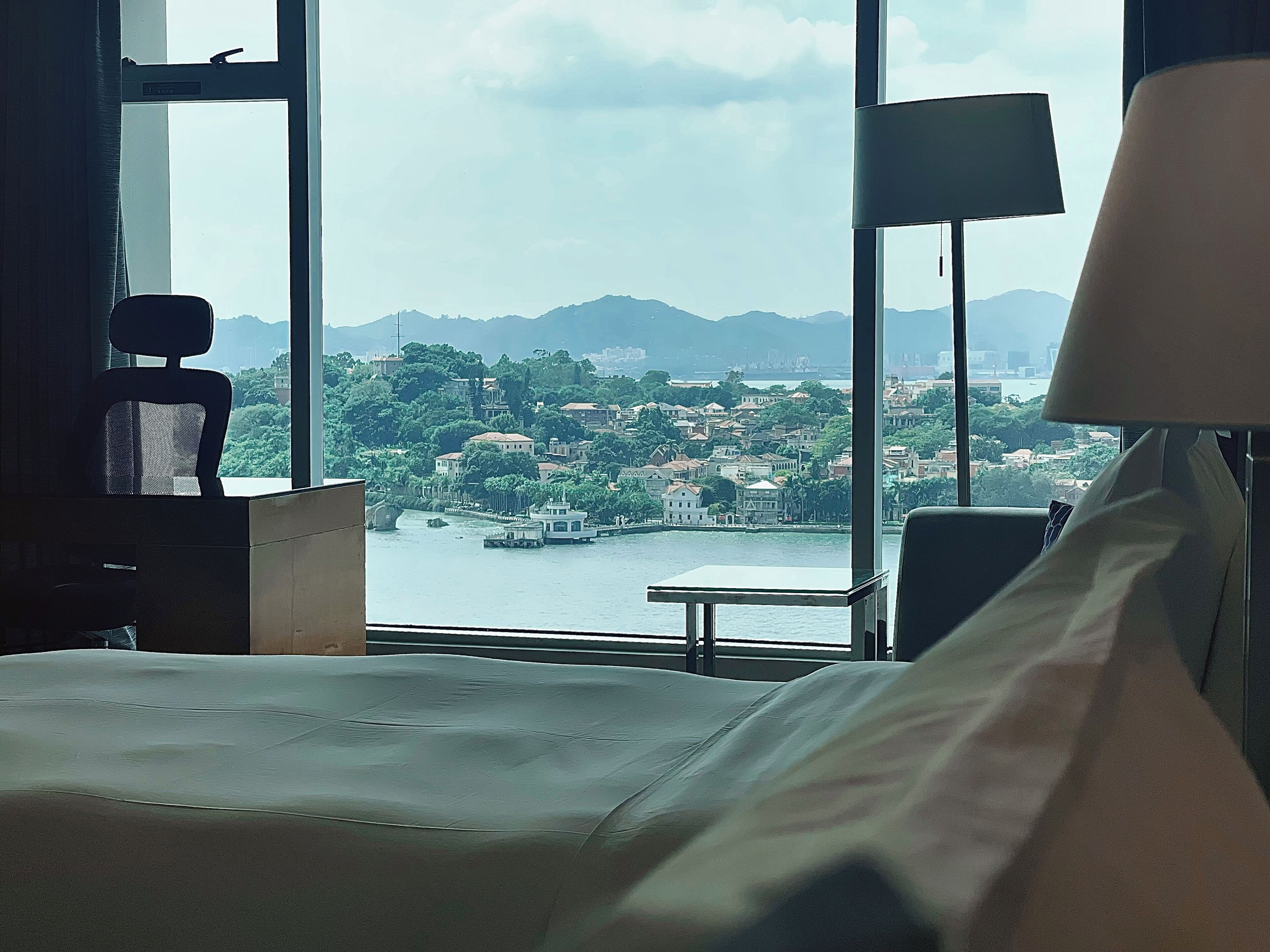 Habitación de hotel con un ventanal grande que ofrece vistas a un paisaje urbano y una masa de agua.