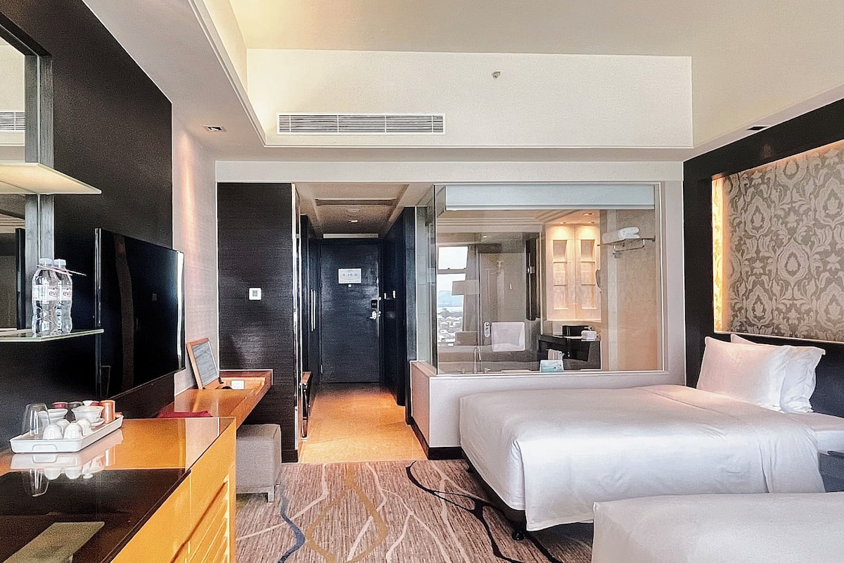 Une chambre d’hôtel avec un lit, un bureau, une télévision et une salle de bain visible à travers une porte ouverte.