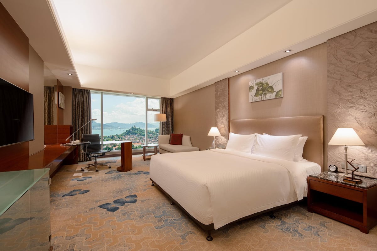 Une chambre d’hôtel avec un grand lit, un bureau, une télévision et une vue sur la ville.