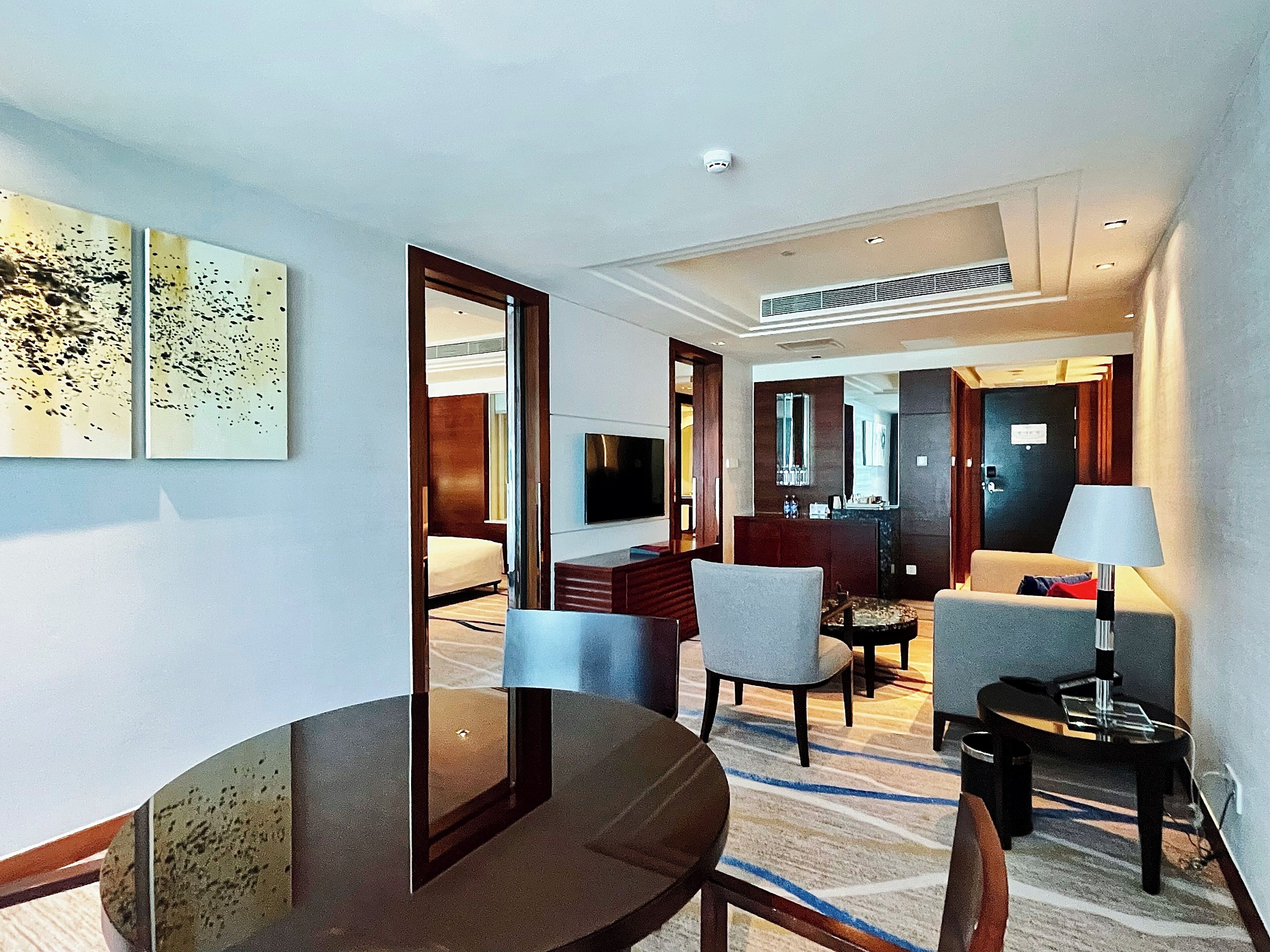 A hotel room with a bed, a TV, a dining table, and a seating area with chairs.