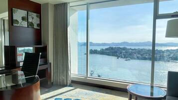 Ein Hotelzimmer mit großem Fenster und Blick auf ein Gewässer sowie die Stadt.