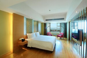 Una habitación de hotel moderna con una cama grande, una mesita pequeña, dos sillas y vistas a la ciudad a través de amplios ventanales.
