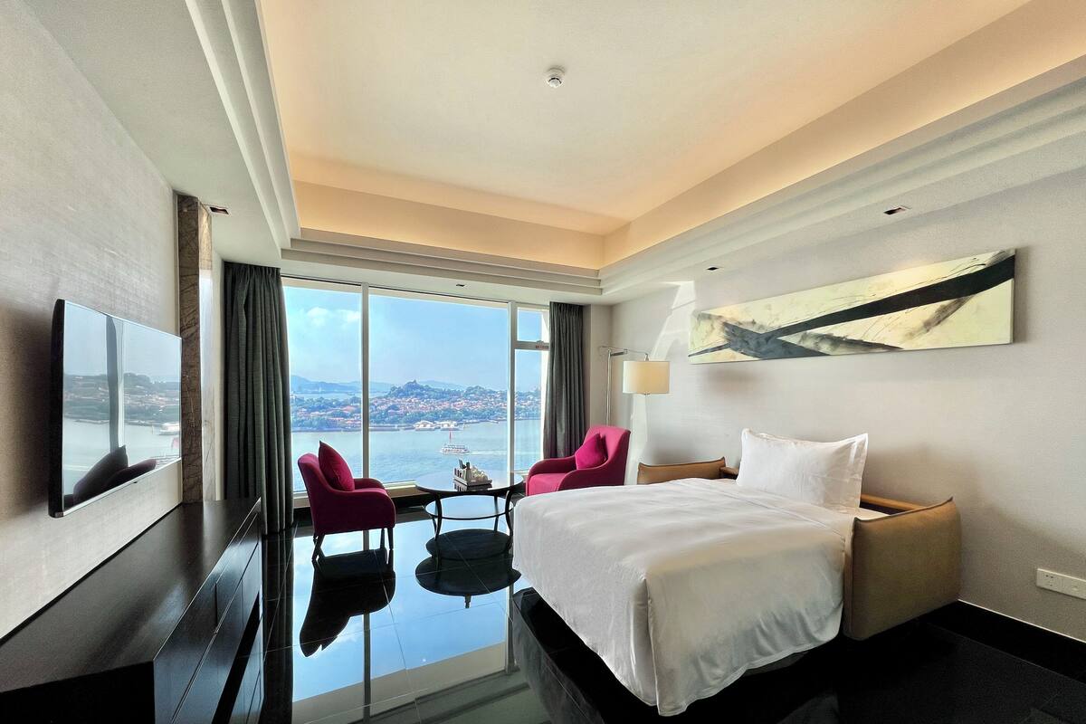 Une chambre d’hôtel équipée d’un lit, d’un bureau, d’une chaise, d’une télévision et offrant une vue sur une étendue d’eau.